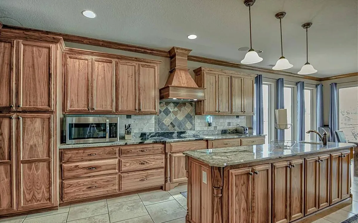 A kitchen scene with wooden cabinetry, granite countertops, an island with seating, and modern appliances. The layout is designed for both cooking and socializing, with ample workspace and intimate seating for group meal prep or casual conversations.