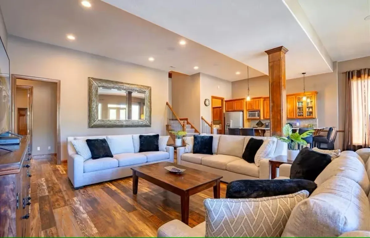 This image showcases a spacious living room with plush sofas, a stylish coffee table, and a view of the adjacent kitchen area. The space feels warm, inviting, and perfect for both casual family gatherings and entertaining guests. The design highlights open-concept living with direct visual flow between the living and kitchen spaces, inviting conversation and connection.