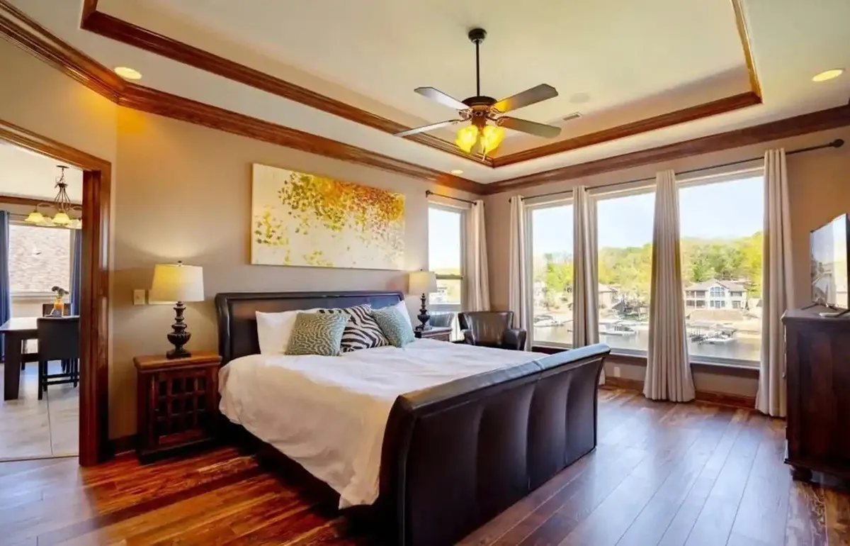 A serene bedroom featuring a king-size bed with plush linens, large windows that offer breathtaking lake views, and tasteful artwork on the walls. Soft natural light streams into the room, creating a tranquil and inviting atmosphere ideal for rest and relaxation.