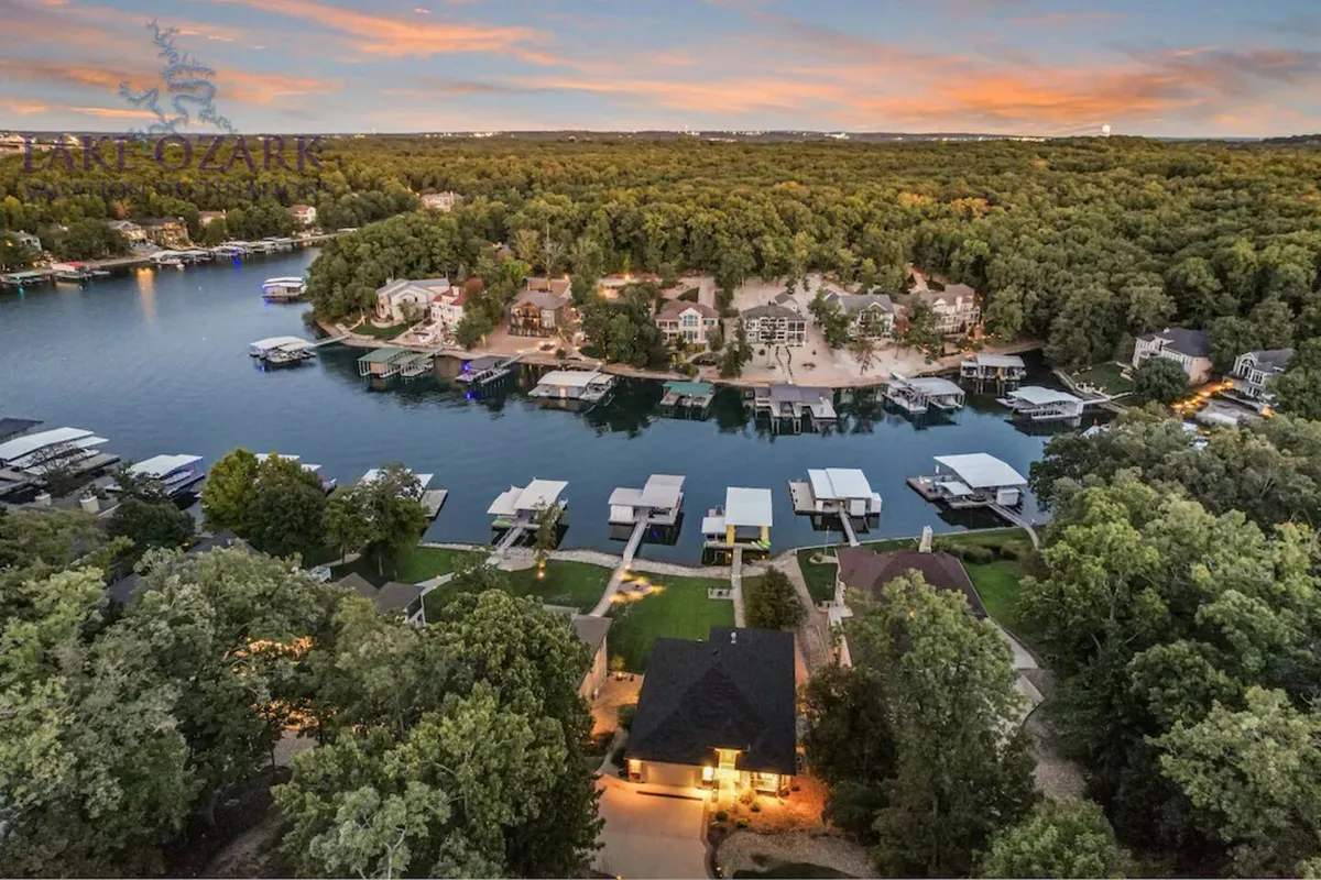 A panoramic view of Lake of the Ozarks showcasing marinas, clustered homes, and lush forested shoreline beneath a glowing sunset sky. The wide perspective sets the scene for boating exploration, with visible docks and expansive water, emphasizing the broader Porto Cima boating lifestyle.