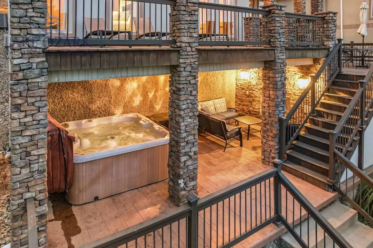 An outdoor space showcasing a luxurious hot tub flanked by stone pillars and comfortable seating, set on a patio. The area is perfect for relaxation and evening gatherings, with an atmosphere of comfort and connection to the outdoors.