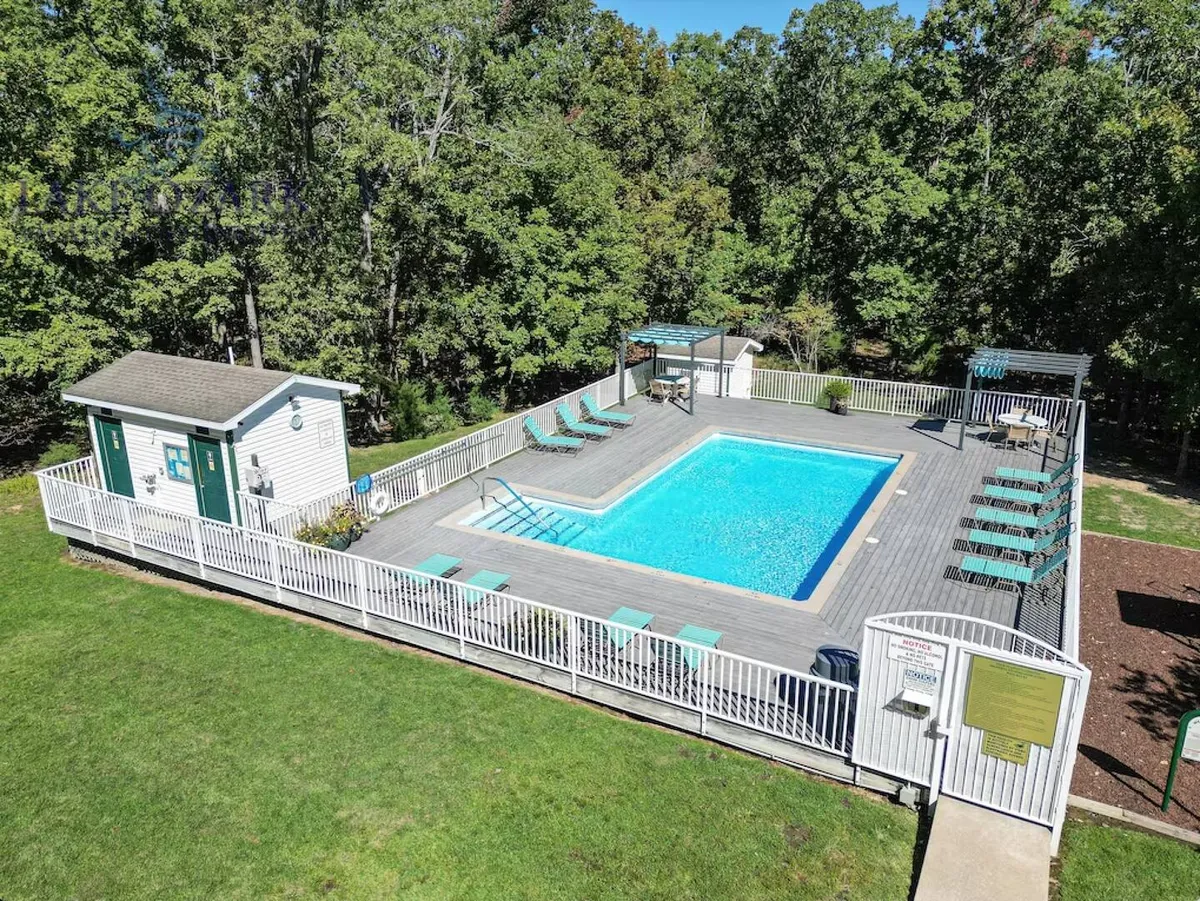 A bright outdoor pool area with lounge chairs, a shower area, and changing rooms, surrounded by greenery. The scene suggests a lively yet relaxed environment perfect for family fun and social gatherings.