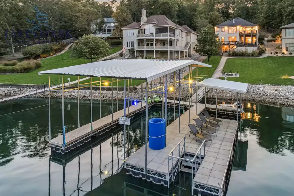 A scenic exterior shot of the private dock extending into the lake, framed by lush lawn and neighboring homes. Water activities such as boating and fishing are implied, with the dock’s large slip and swim platform clearly visible.