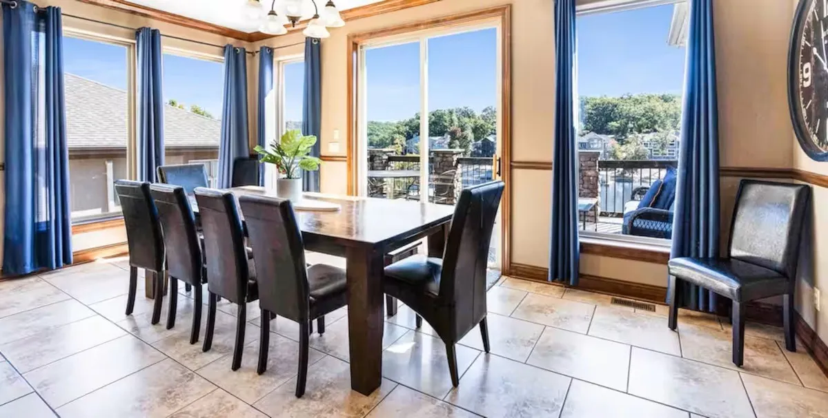 This image features a formal dining area with a large table set by expansive windows dressed in blue curtains. The space is bathed in natural light, offering a scenic view—ideal for family gatherings, festive dinners, or relaxed brunches. The setting is elegant yet approachable, matching the tone of memorable meals mentioned in the section.