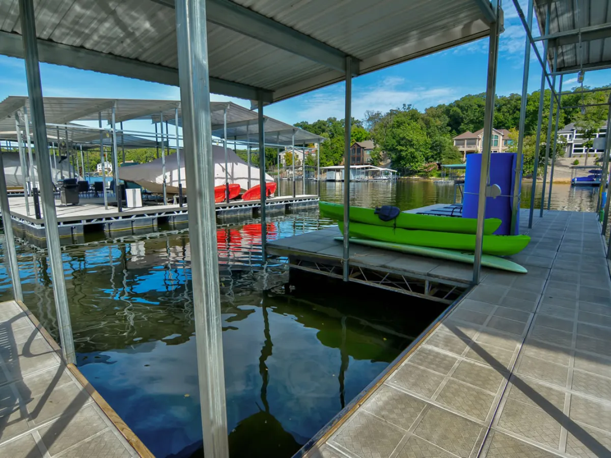 A vibrant lakefront dock scene featuring a green kayak and red boats resting at the dock, with calm water reflecting the clear sky and lush greenery all around. The dock structure extends into the gentle cove, evoking a sense of adventure and tranquility.