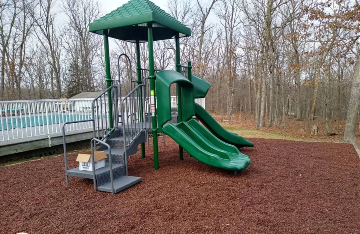 A bright, inviting playground structure with slides, surrounded by leafy trees. The play area radiates energy and fun, ideal for children and families to gather and play in a safe, natural setting.