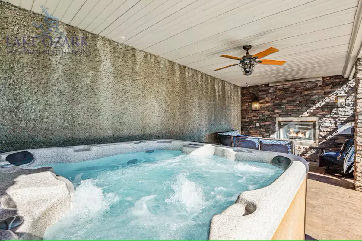 An inviting interior scene featuring a hot tub surrounded by stone walls and a cozy fireplace, with plush seating nearby. The setting is tranquil and ideal for both relaxation and socializing after a day on the lake.