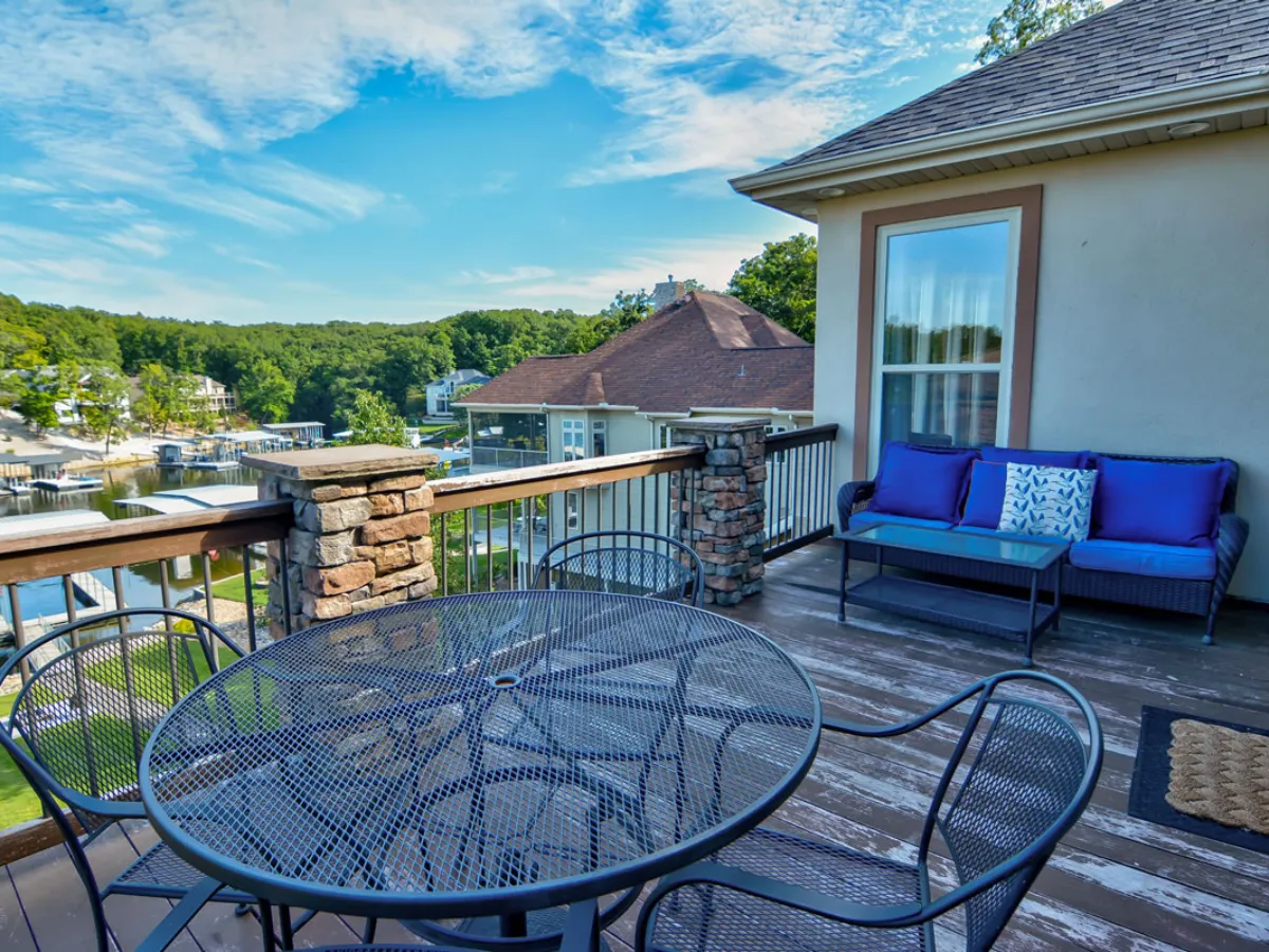 An inviting outdoor patio with a table and chairs set, plush couch with pillows, and a scenic view of the lake beyond. The space is perfect for outdoor dining, gathering with friends, or simply enjoying sunrise coffee or sunset cocktails while taking in the expansive lake views.