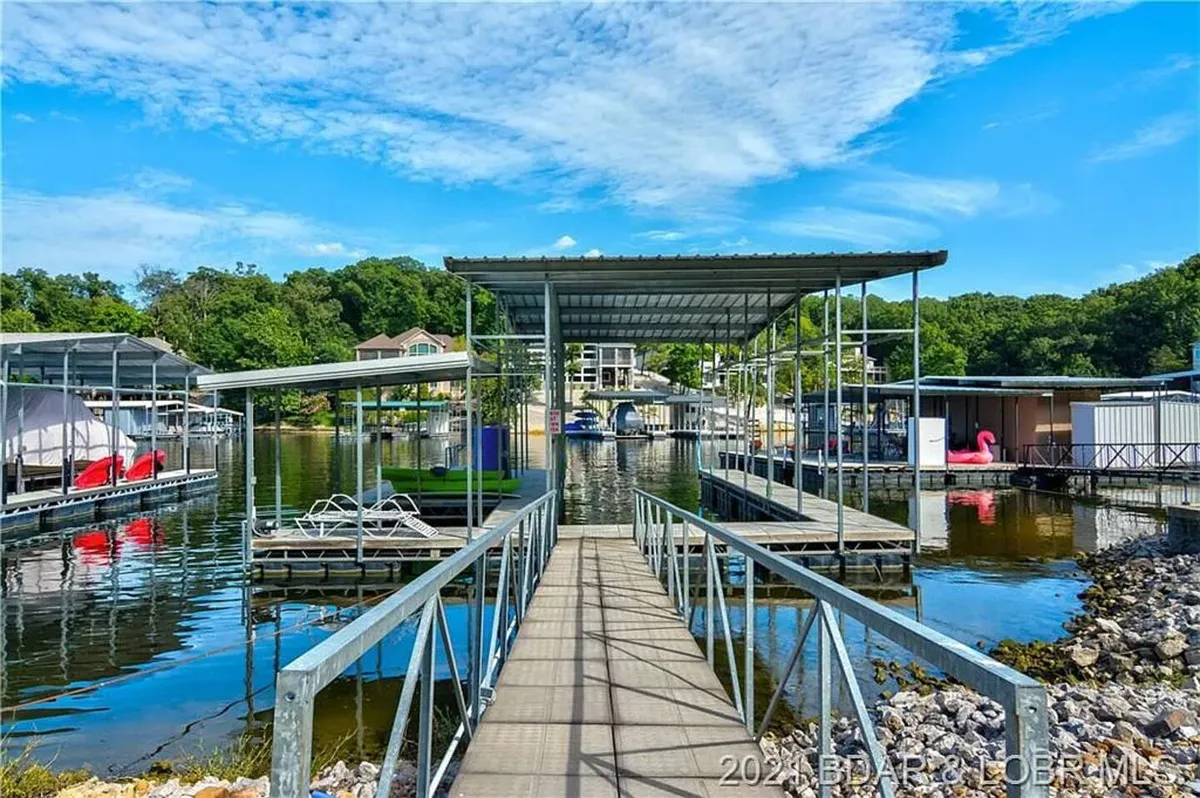 A serene exterior scene capturing a private dock extending into the calm lake, flanked by boathouses and lush green foliage. The water is inviting, with ample space for mooring boats and enjoying water activities. The quiet, sheltered setting suggests a perfect environment for both relaxation and active boating pursuits.
